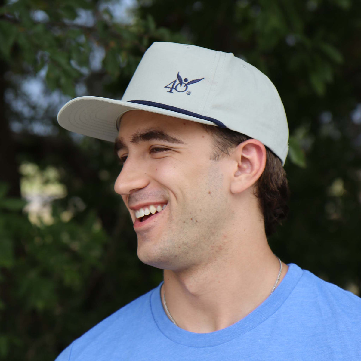 Man wearing a light gray cap with a logo, smiling outdoors.