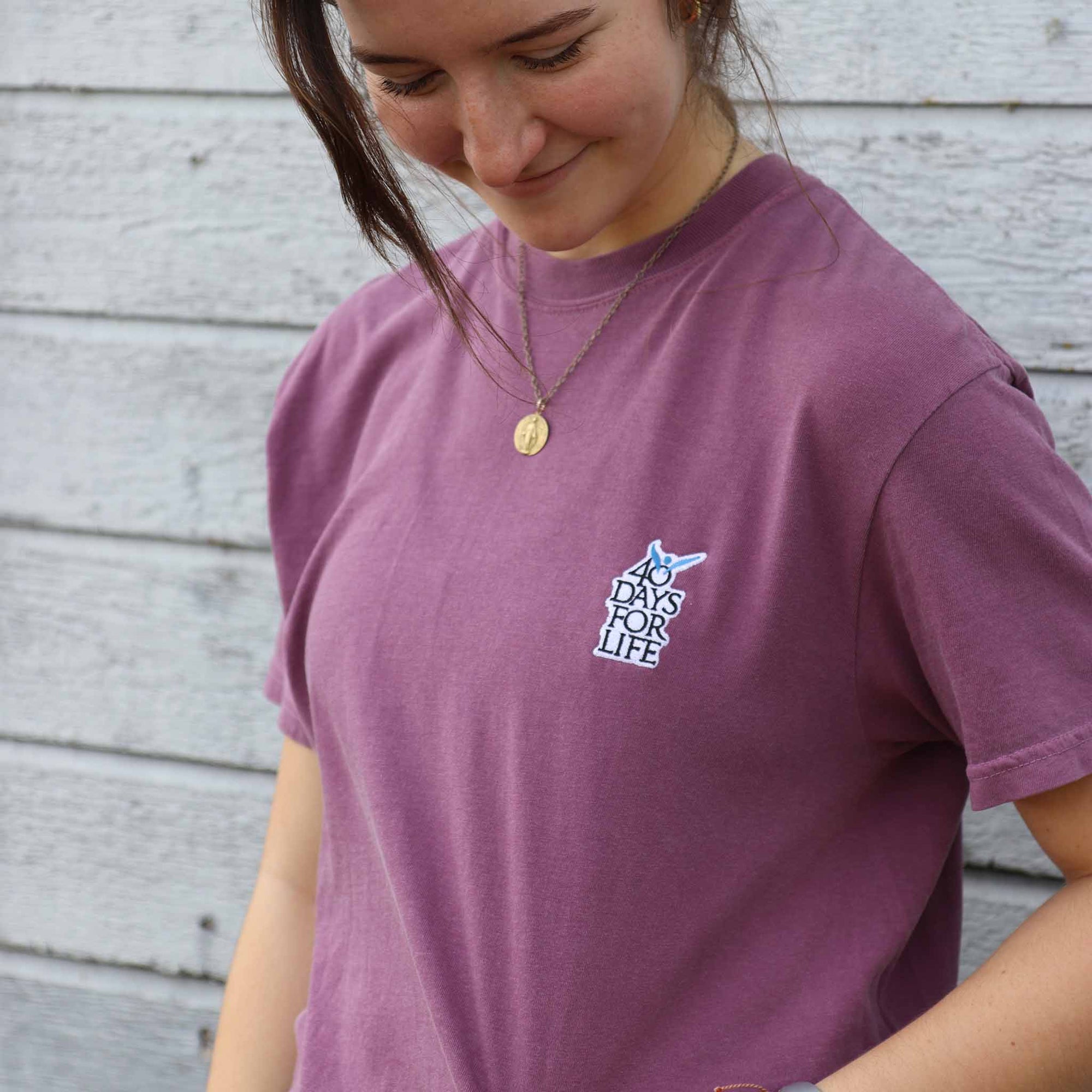 Female wearing a purple t-shirt with a 40 Days for Life logo, standing against a wooden wall.