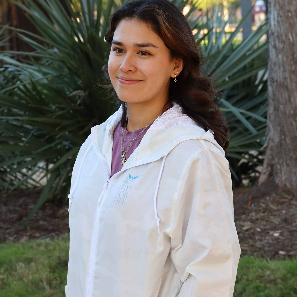 Woman wearing a white windbreaker with 40 Days for Life logo standing outdoors with greenery in the background