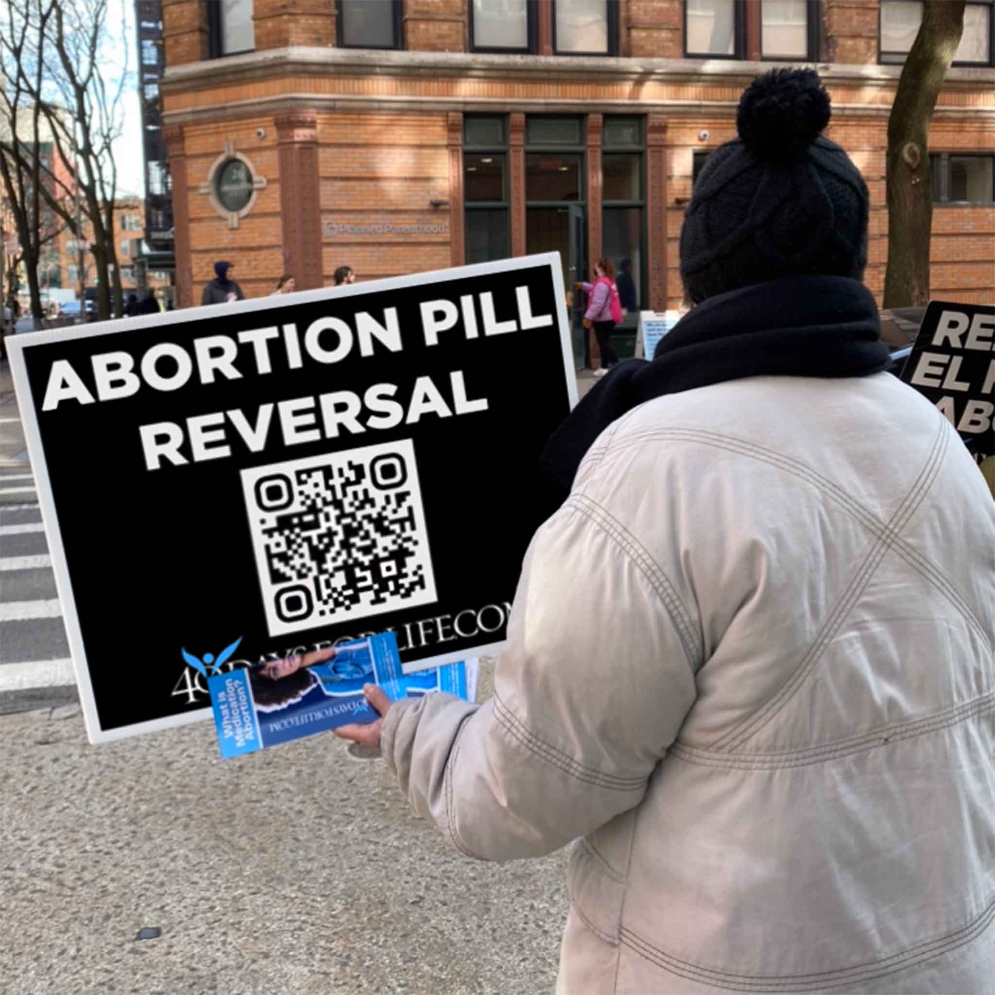 Person holding a 40 Days for Life sign for abortion pill reversal in an urban setting